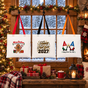 Three Christmas 2027 cotton tote bags with red, black and orange handles hanging in front of a snowy cabin window with gingerbread, gold Happy New Year 2027 and gnome prints