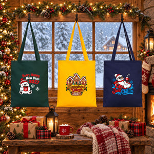 Three Christmas 2027 cotton gabardine tote bags in forest green, golden yellow and navy blue hanging in front of a snowy cabin window with polar bear, gingerbread village and snowman prints