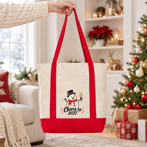 Hand lifting a red strap canvas tote bag with a snowman Cheers to 2027 print in a bright Christmas living room