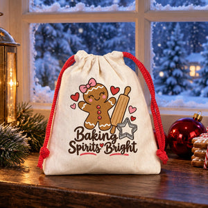 Cotton pouch with a red cord printed with a Baking Spirits Bright gingerbread design on a windowsill with a candle lantern, gingerbread cookies and a snowy garden behind