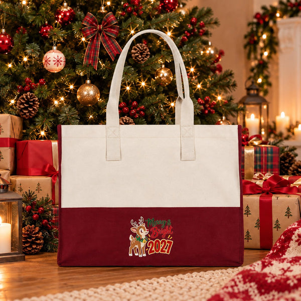 Burgundy canvas tote bag with a Merry and Bright 2027 reindeer print standing on a wooden floor under a decorated Christmas tree among wrapped gifts