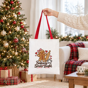 Red handle cotton tote bag with a Baking Spirits Bright gingerbread print held by hand in a bright Christmas living room