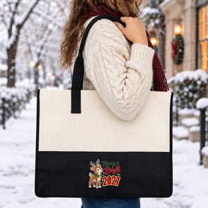Woman in a cream cable-knit wool sweater and burgundy scarf carrying the black canvas tote bag with a Merry and Bright 2027 reindeer print on her shoulder on a snowy winter street