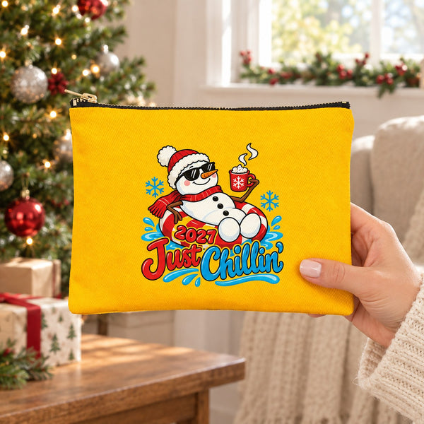 Hand in a cream knit sweater holding a yellow clutch with a 2027 Just Chillin snowman print in a festive living room, showing the real size