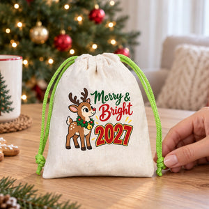 Cotton pouch with a green cord printed with a Merry and Bright 2027 fawn design on a table, a hand holding the knotted cord end to show the real palm size