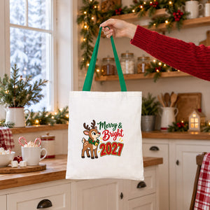 Green handle cotton tote bag with a Merry and Bright 2027 reindeer print held by hand in a cosy Christmas kitchen