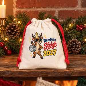 Cotton pouch with a red cord printed with a Ready to Sleigh 2027 reindeer on a rustic mantel with a lit garland, candles and knitted Christmas stockings, a stocking stuffer gift bag