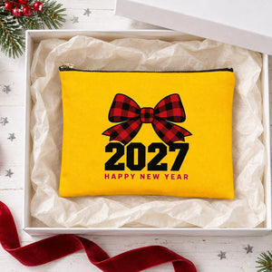 Yellow clutch bag with a buffalo plaid bow 2027 Happy New Year print in an open white gift box with tissue paper, ribbon and ornaments