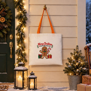 Cotton tote bag with orange handles and a gingerbread Merry Christmas and Happy New Year 2027 print hanging by a snowy front door