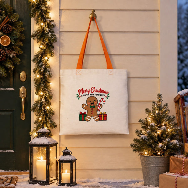Cotton tote bag with orange handles and a gingerbread Merry Christmas and Happy New Year 2027 print hanging by a snowy front door