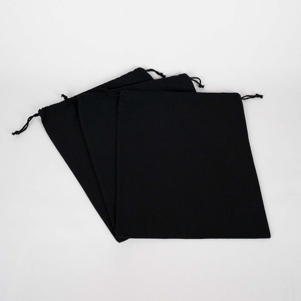 Real photo of three plain black cotton drawstring bags lying flat, showing the drawstring cords