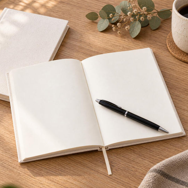 Open blank canvas notebook with pen next to a coffee cup and eucalyptus on a wood desk | Pamusan.com