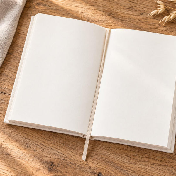 Blank canvas notebook open on a wood desk showing unlined cream pages and ribbon bookmark | Pamusan.com